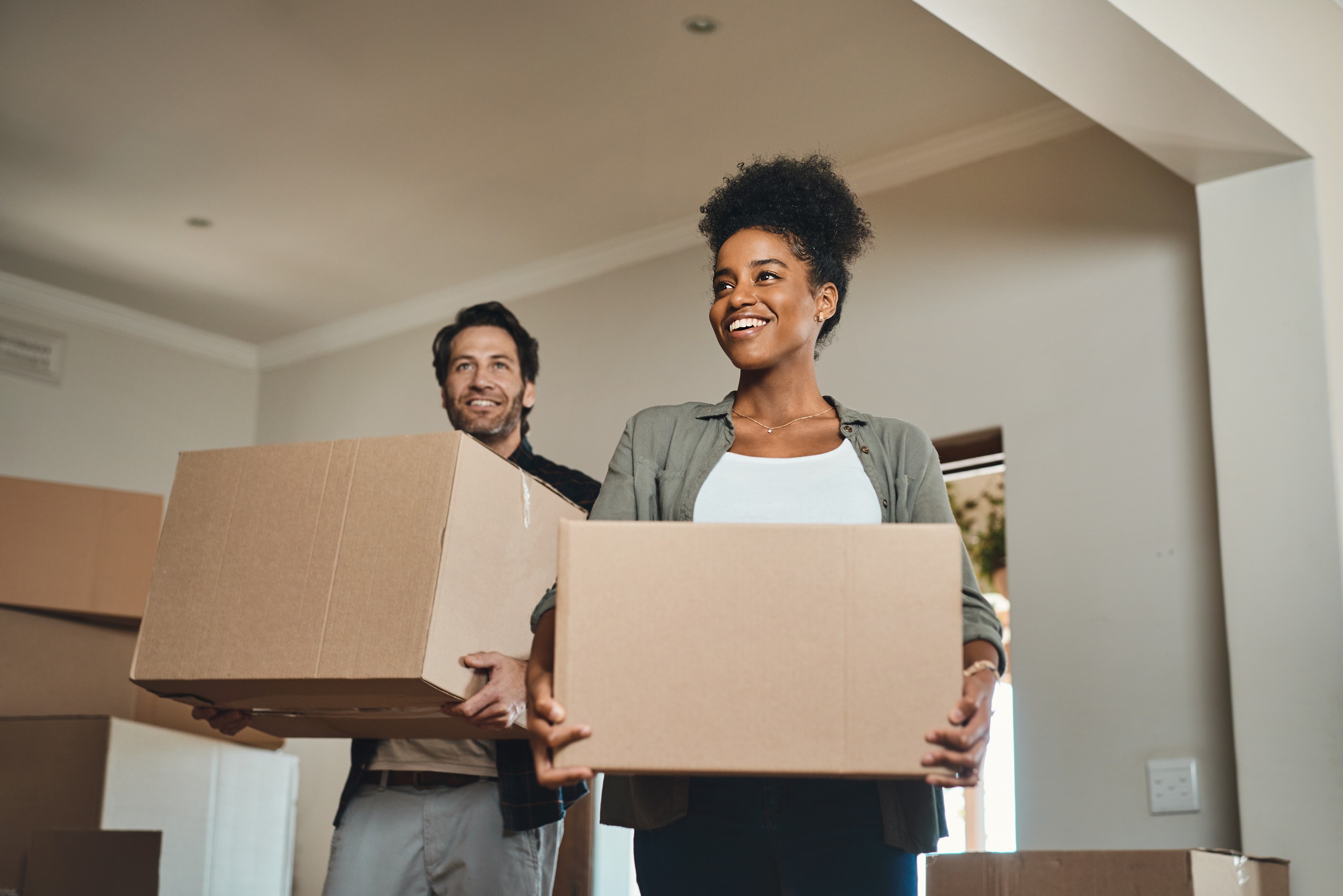 Two happy people moving boxes into a house.