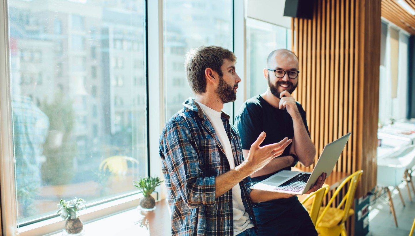 People in business casual setting talking near laptop