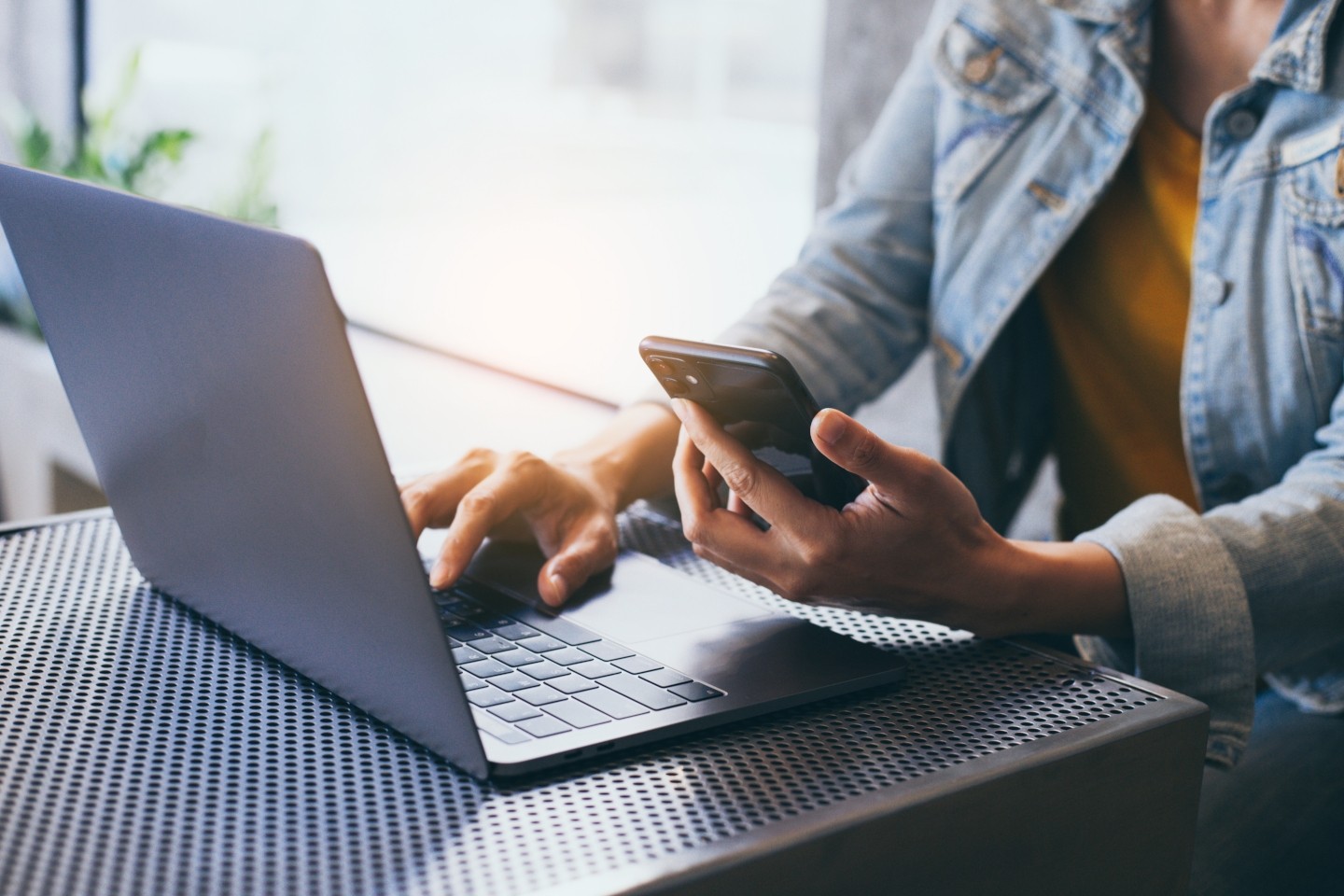 Person at laptop typing while looking at phone